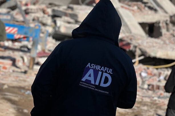 An Ashraful Aid team member standing in front of earthquake rubble during a disaster response