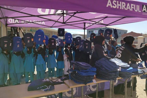 Learners holding up new school bags at an Ashraful Aid school support distribution