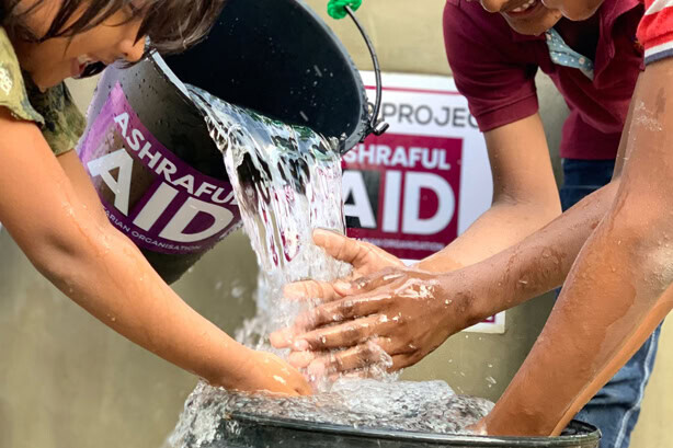 Clean water being poured from an Ashraful Aid bucket over children’s hands