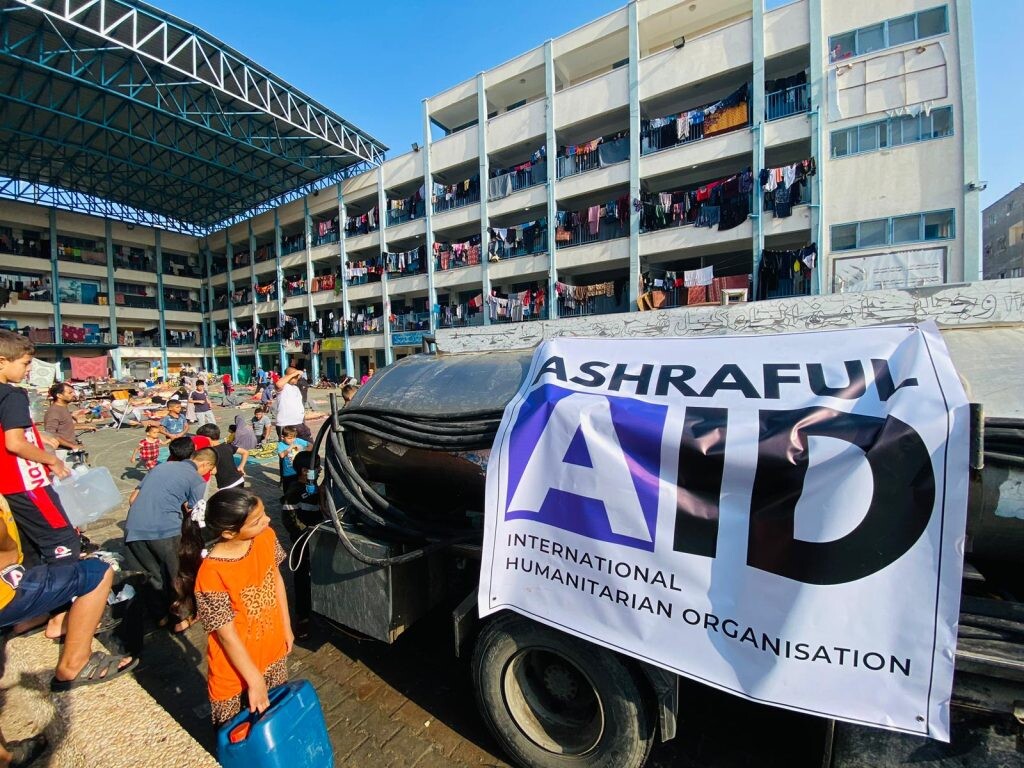 Displaced families collecting water from an Ashraful Aid tanker in the courtyard of a school shelter in Gaza