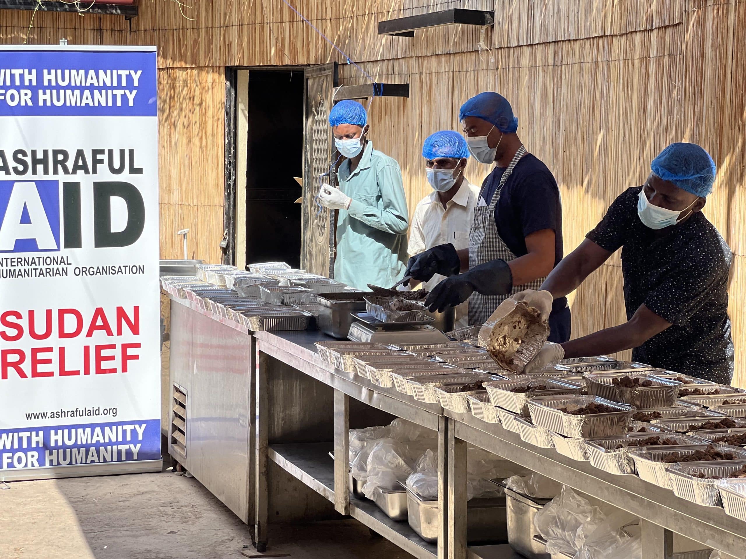 Ashraful Aid kitchen team in hairnets and masks packing hot meals into foil trays for Sudan relief